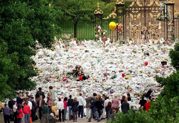 People gathering in front of a mass of flowers placed in front of Kensington Palace